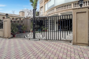 Una entrada cerrada con un portón de hierro decorativo, plantas en macetas y un camino pavimentado.