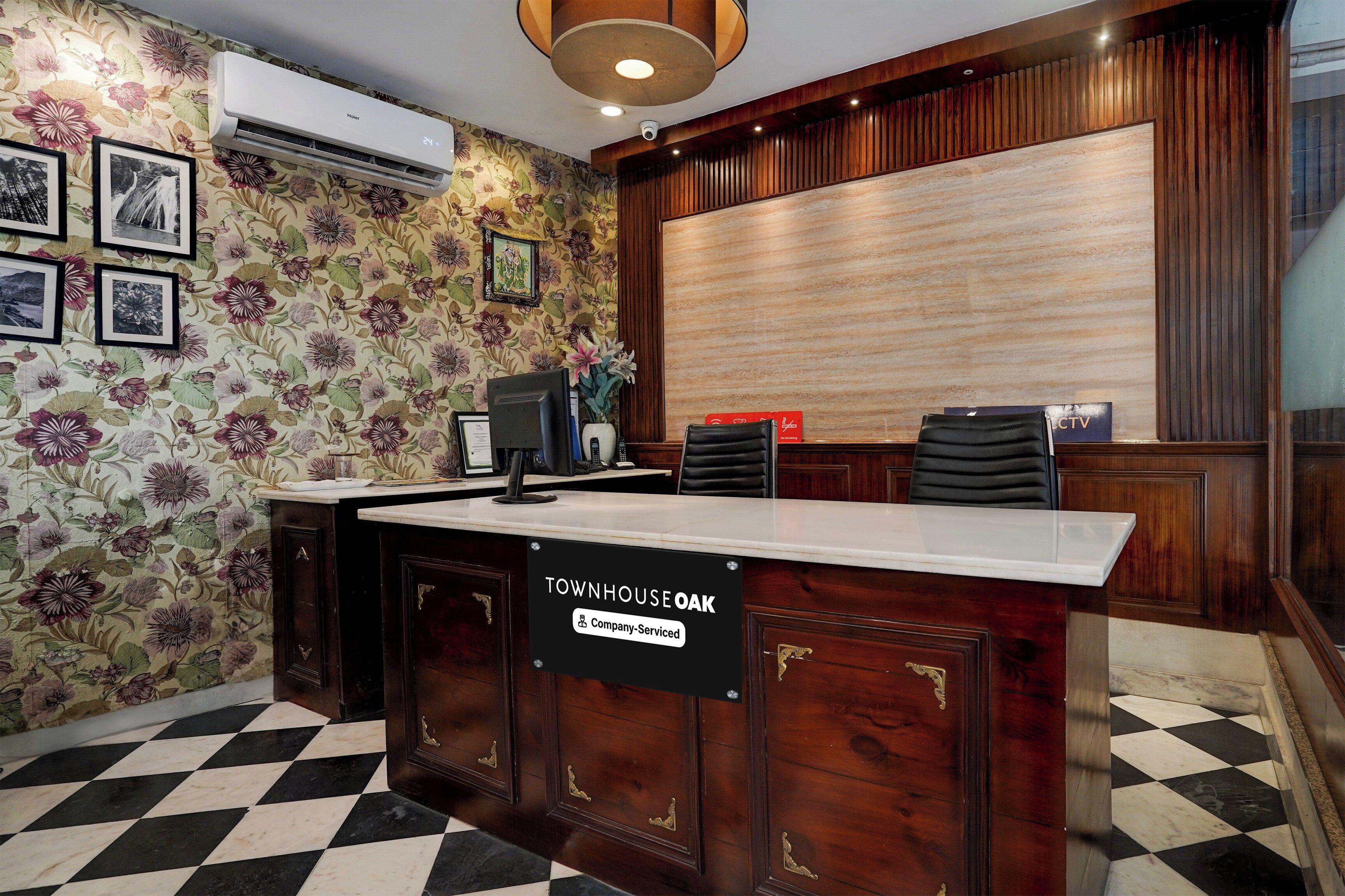 A reception desk with a sign indicating it is company-serviced, a floral wallpaper, a black and white checkered floor, and a wooden panel wall.