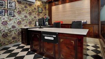 A reception desk with a sign indicating it is company-serviced, a floral wallpaper, a black and white checkered floor, and a wooden panel wall.
