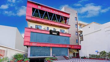 A hotel building with a prominent red and white facade, a sign indicating it's a hotel, and a checkered pavement area with potted plants.