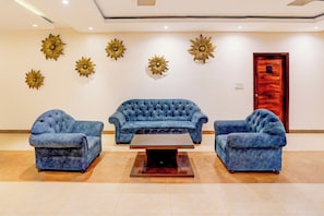Uma área de recepção com um sofá azul, duas poltronas, uma mesa de centro e detalhes decorativos nas paredes.