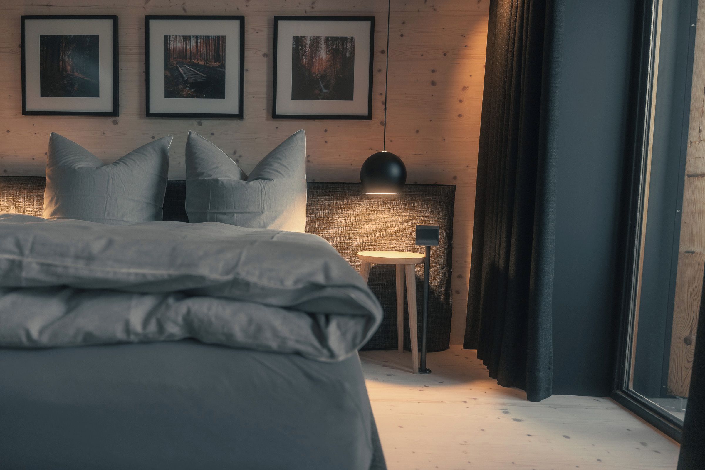 Ein Schlafzimmer mit einem Bett, Kissen, einem Nachttisch, einer Lampe und gerahmten Bildern an der Wand.