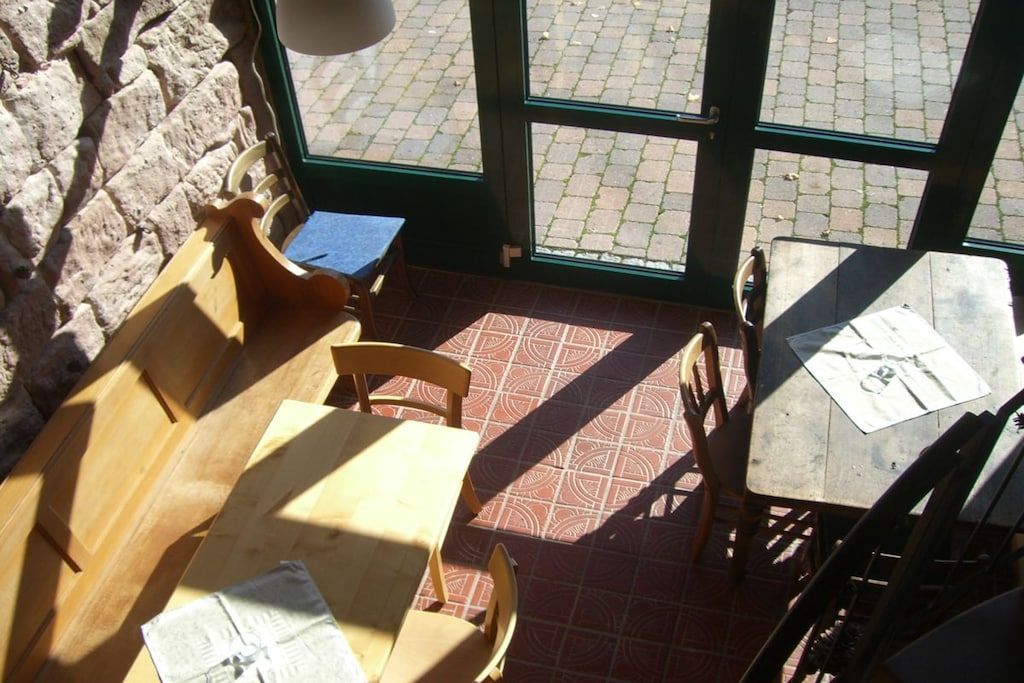 An indoor seating area with tables and chairs, a stone wall, and a view through a glass door.