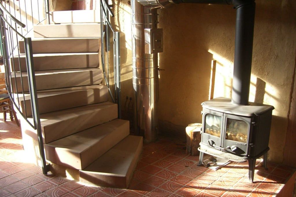 A staircase with a metal handrail, a wood-burning stove, and a tiled floor.