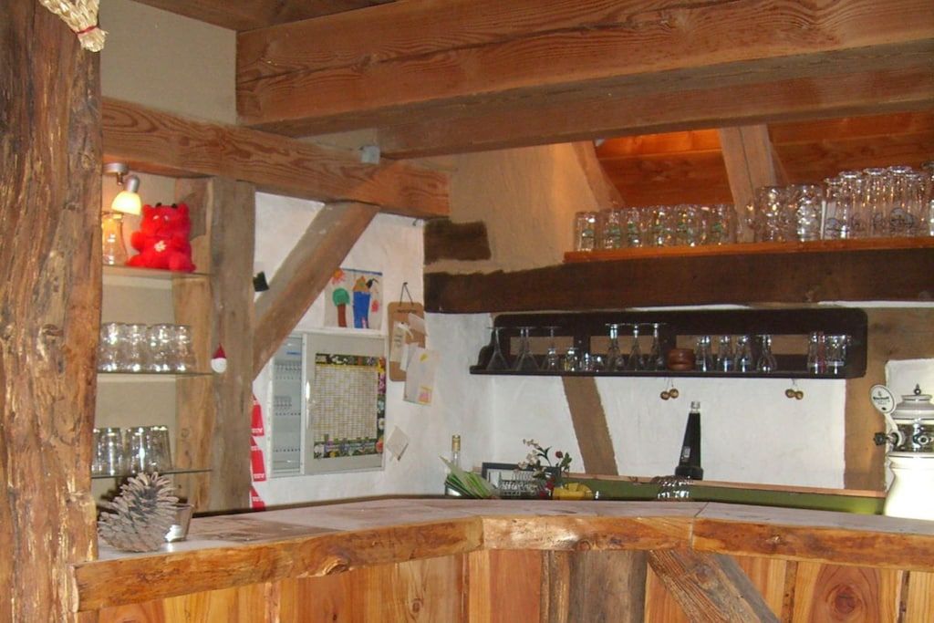 A rustic wooden bar area with shelves holding glasses and bottles, a red teddy bear decoration, and a vintage coffee machine.