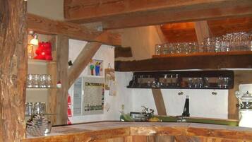 A rustic wooden bar area with shelves holding glasses and bottles, a red teddy bear decoration, and a vintage coffee machine.