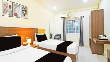 A hotel room with two beds, a desk, a chair, a window with curtains, and wall art.
