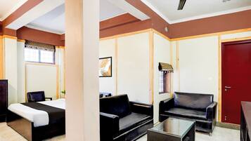 A hotel room with a bed, a sofa, a coffee table, a chair, a red door, and a ceiling fan.