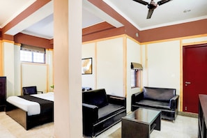 Habitación de hotel con cama, sofá, mesa de centro, silla, puerta roja y ventilador de techo.