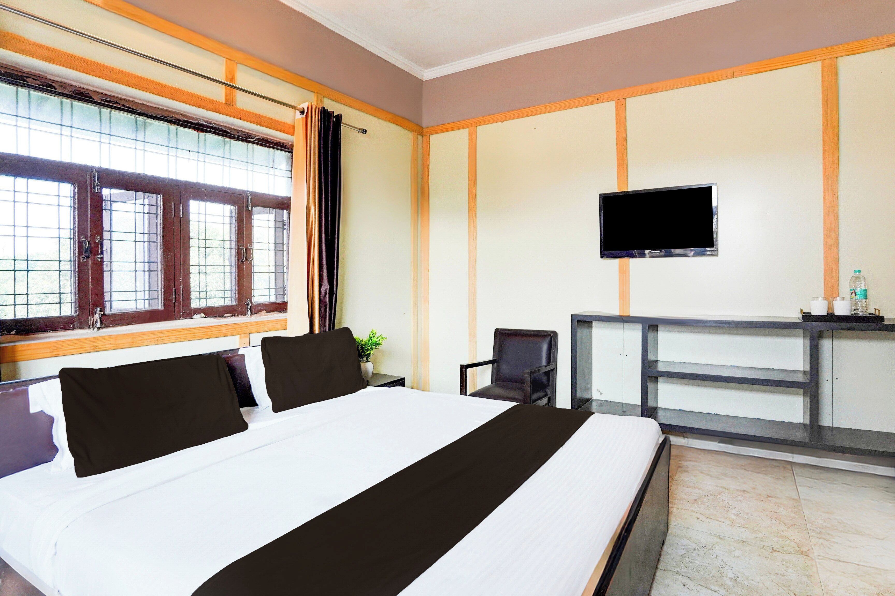A hotel room with a bed, a desk, a chair, a TV, and a window with curtains.