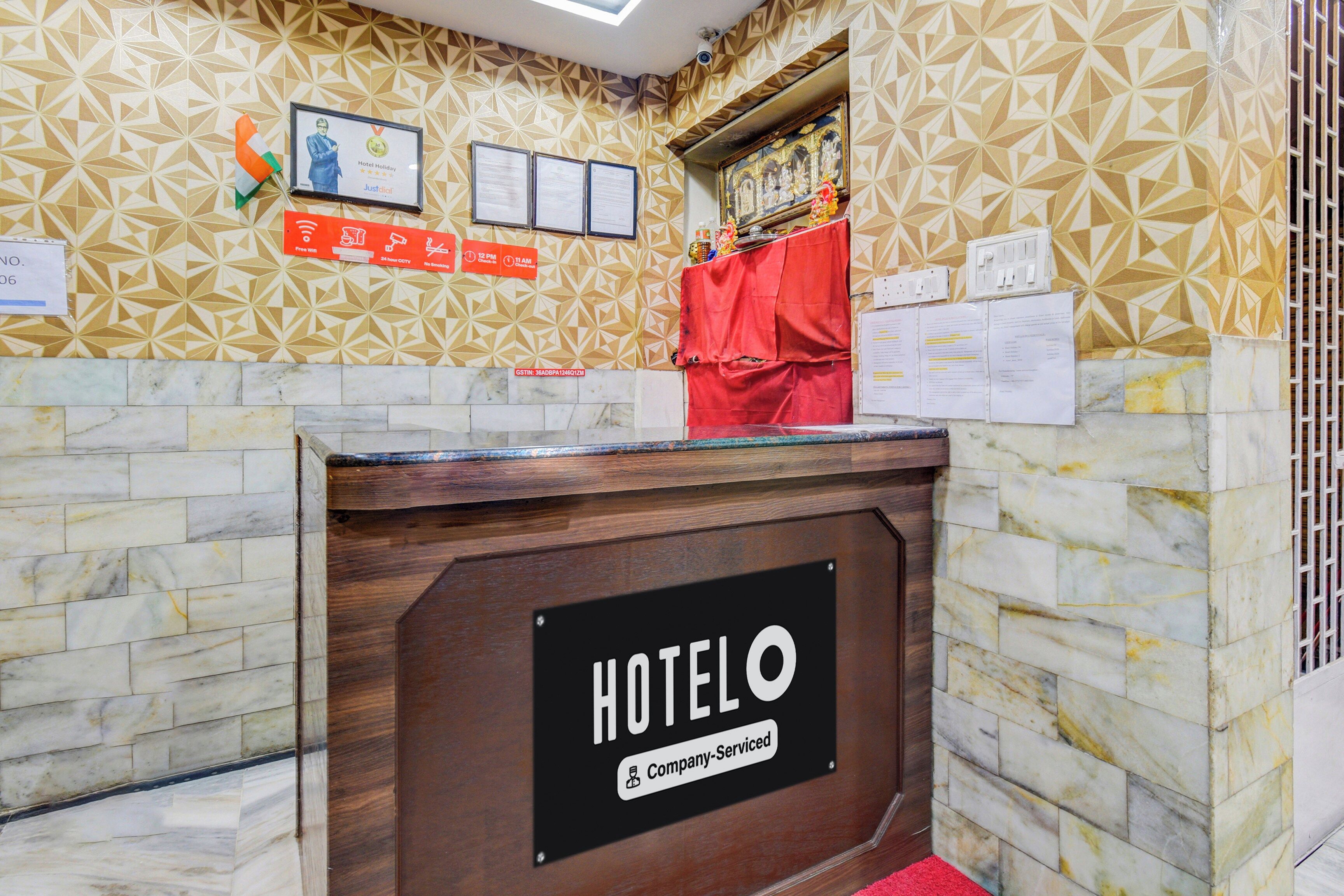 A hotel reception desk with a geometric patterned wall, a framed certificate, and various informational signs.