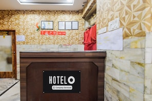 Taulell de recepció d'hotel amb un senyal que indica servei de l'empresa. Hi ha diplomes emmarcades a la paret, un teixit vermell penjant i diversos documents clavats a la paret.