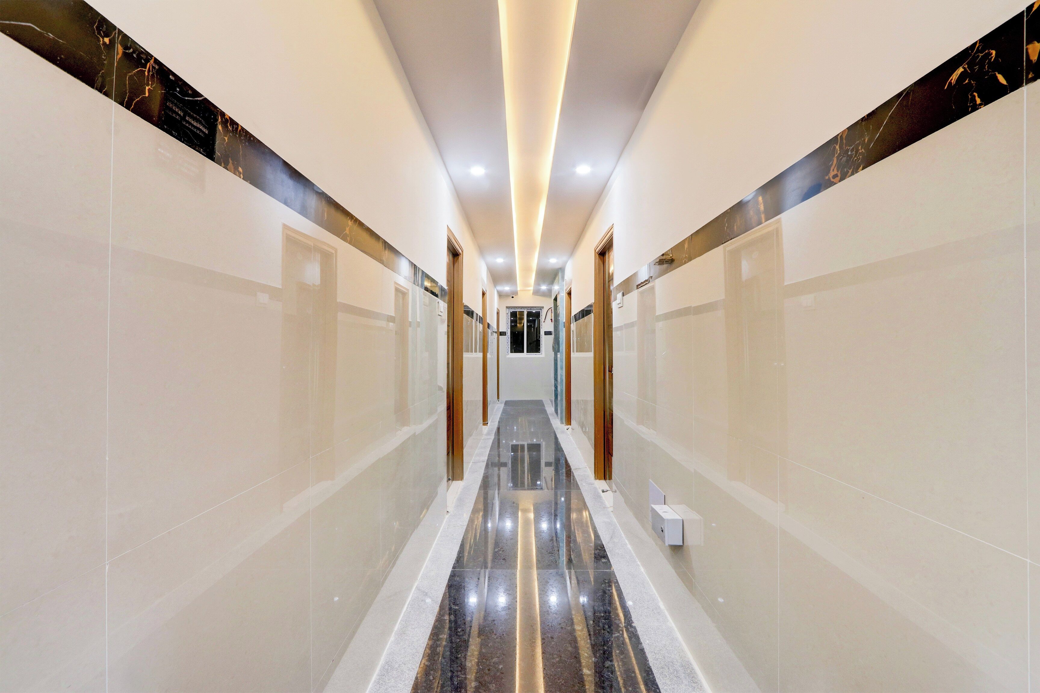 A corridor with reflective flooring and walls, leading to a door at the end.