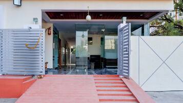 Entrada de um edifício moderno com porta de vidro, tapete vermelho e portão de metal.