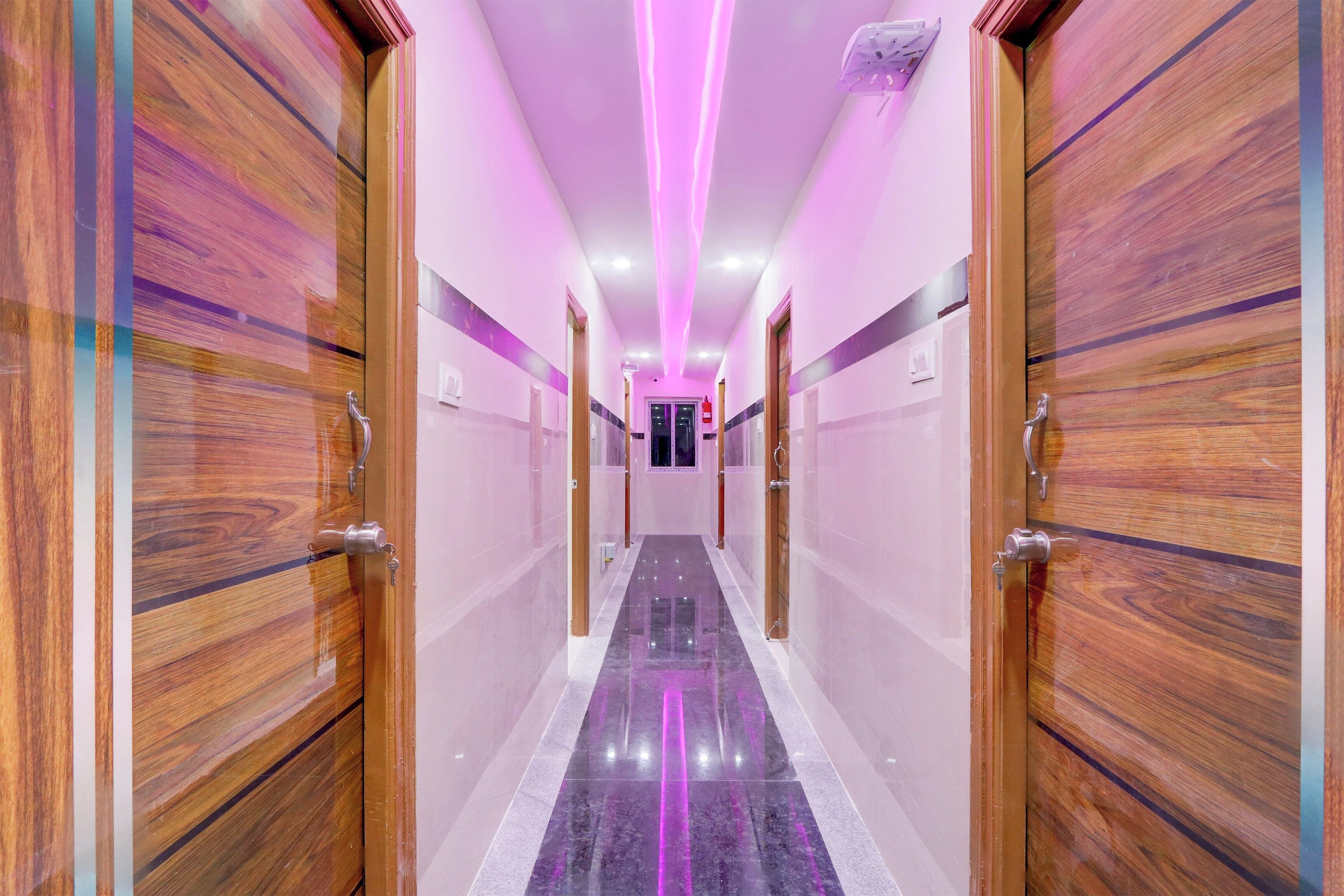 A hallway with wooden doors and a marble floor, leading to a room with a window.