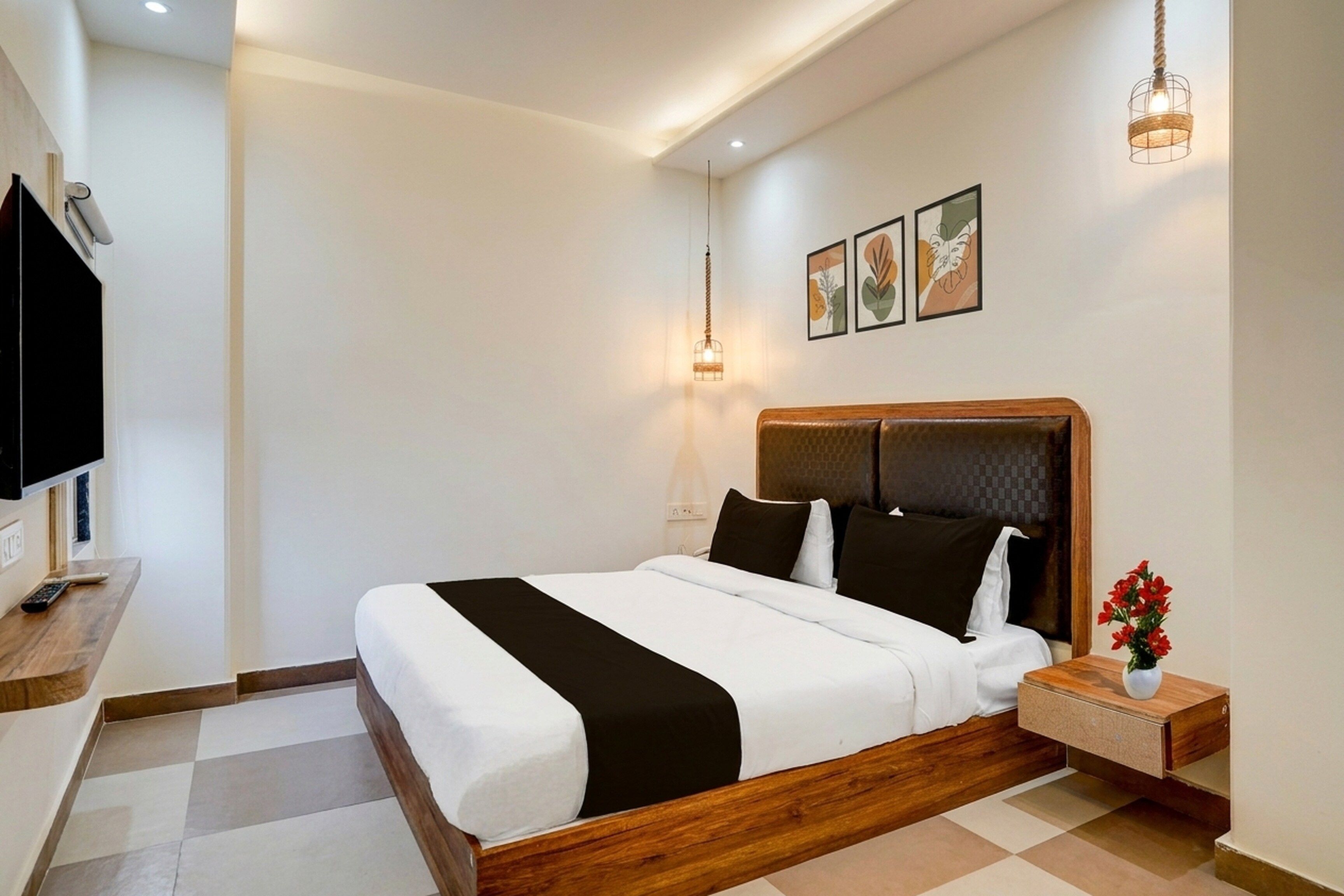 A hotel room with a bed, a bedside table with a vase of flowers, a television, and artwork on the wall.