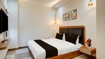 Quarto de hotel com cama, mesa de cabeceira com um vaso de flores, televisão e uma obra de arte na parede.