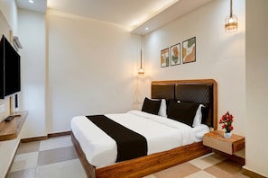 Ein Hotelzimmer mit einem Bett, einem Nachttisch mit Blumenvase, einem Fernseher und Kunstwerken an der Wand.