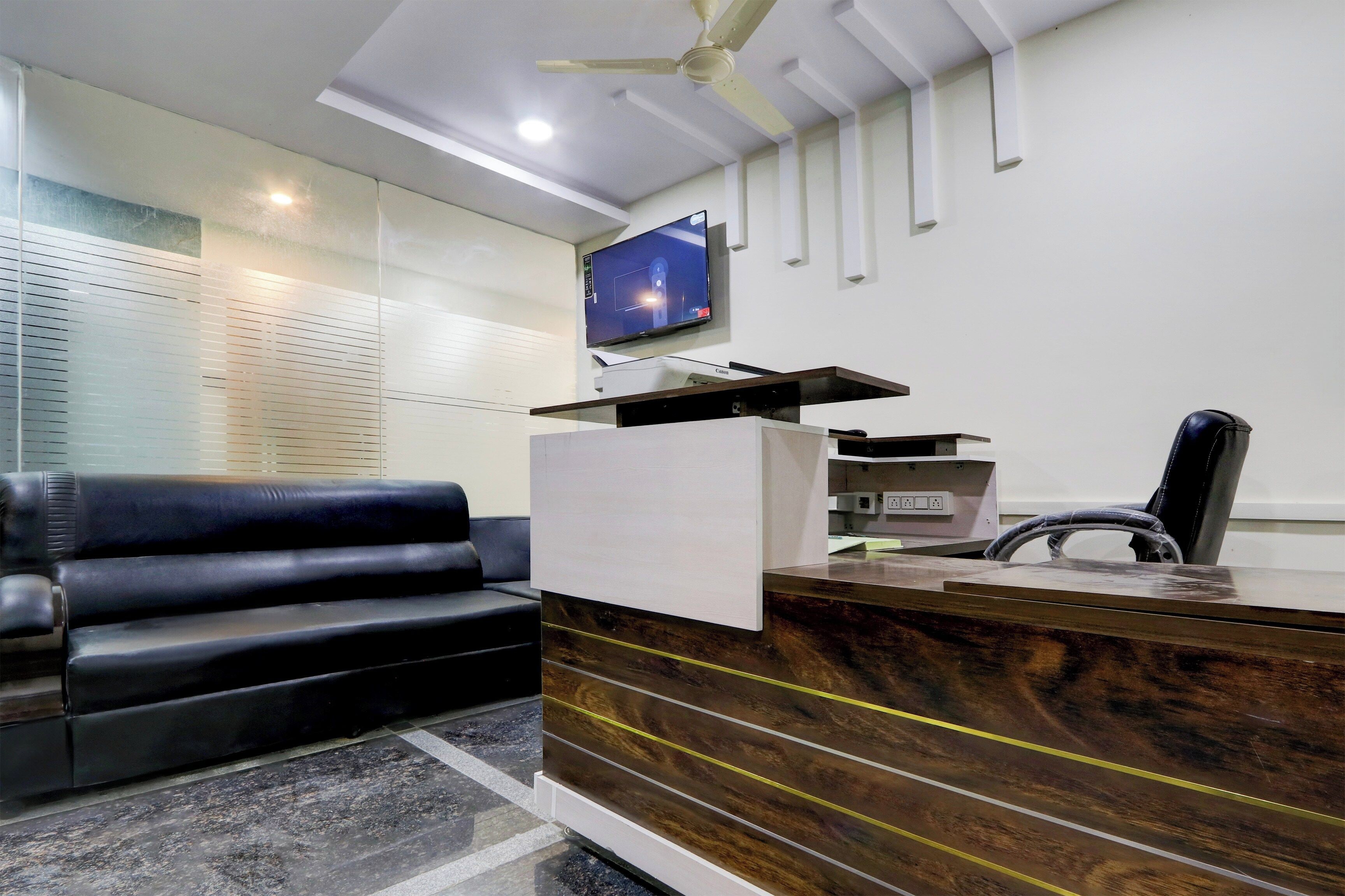 Un área de recepción con un sofá de cuero, un mostrador de madera, un televisor de pantalla plana en la pared y un ventilador de techo.