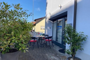 An outdoor seating area with tables and chairs, a potted plant, and a building with a glass door. - Holiday apartment with 1 bedroom (Konstanz)