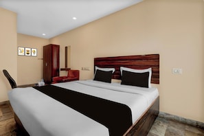 Habitació d'hotel amb llit, una poltrona vermella, un armari de fusta i una obra d'art penjada a la paret.