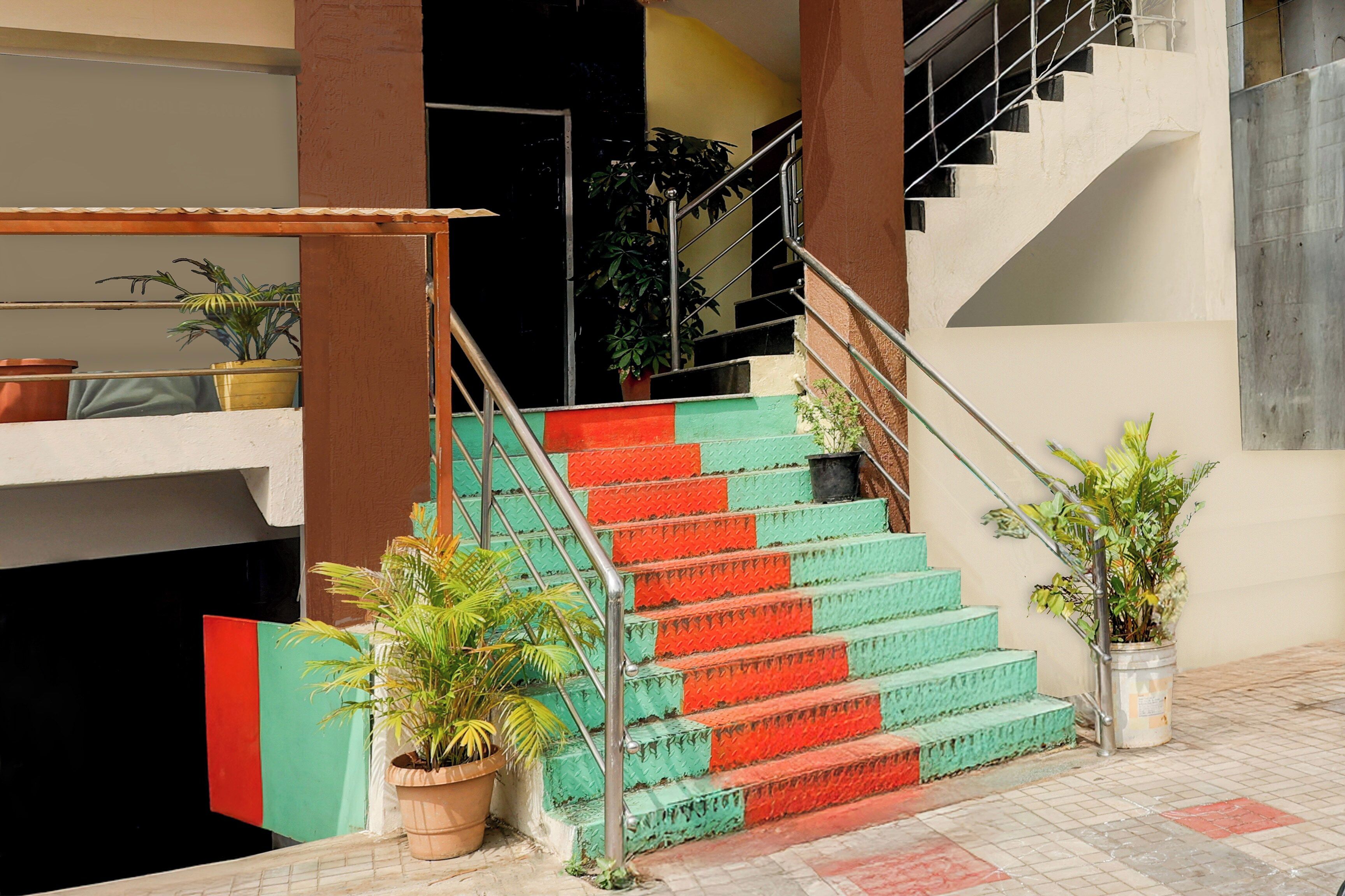 A staircase with alternating red and green steps, metal railings, and potted plants at the base.