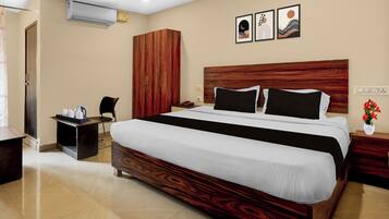 Habitación de hotel con una cama grande, cabecera de madera, escritorio con silla, armario y aire acondicionado de pared.