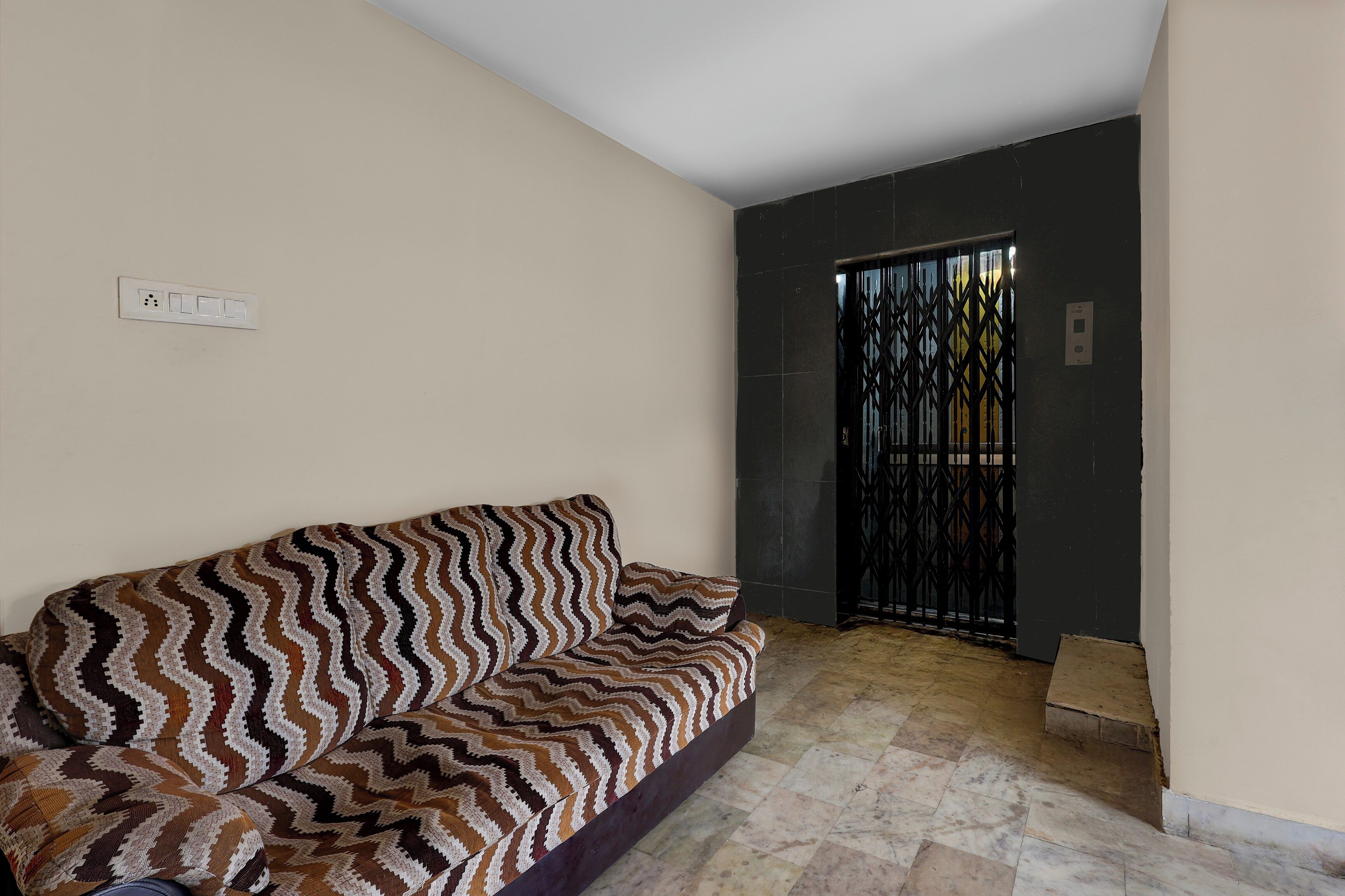 A room with a patterned sofa, a tiled floor, and a door with a metal gate.