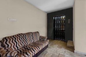 Una habitació amb un sofà estampat, un terra de rajola i una porta amb reixa de metall.