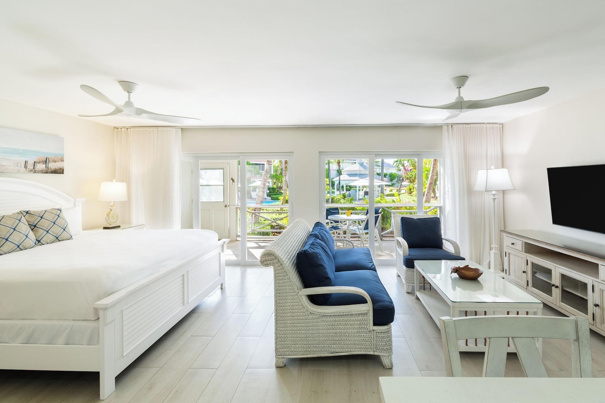 Habitación de hotel con cama, sofá, mesa de comedor y televisor. Posee un balcón con vistas al exterior.