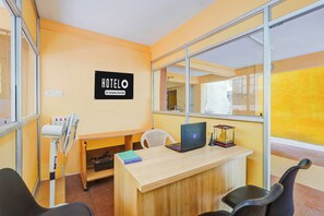Een hotelkamer met een bureau, een stoel, een laptop, een ventilator en een bordje dat aangeeft dat de kamer dienstverlenend is voor bedrijven.