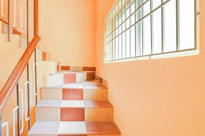 A staircase with alternating red and white tiles, a wooden handrail, and a window with metal bars. - Hotel O Velachery Near Devi (Chennai)