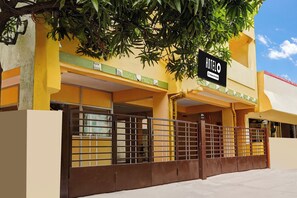 A hotel entrance with a metal gate, a signboard, and a tree overhead. - Hotel O Velachery Near Devi (Chennai)
