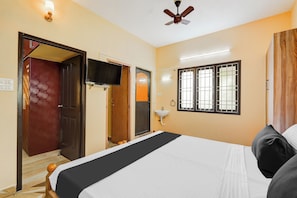 Een hotelkamer met een bed, een televisie, een plafondventilator, een raam met tralies en een deur.