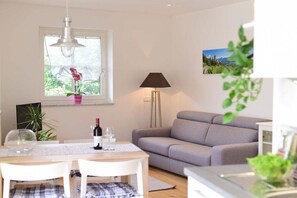 A modern living room with a grey sofa, a dining table with chairs, a lamp, and a window with a view of greenery. - Holiday apartment in Merano with swimming pool (Meran)