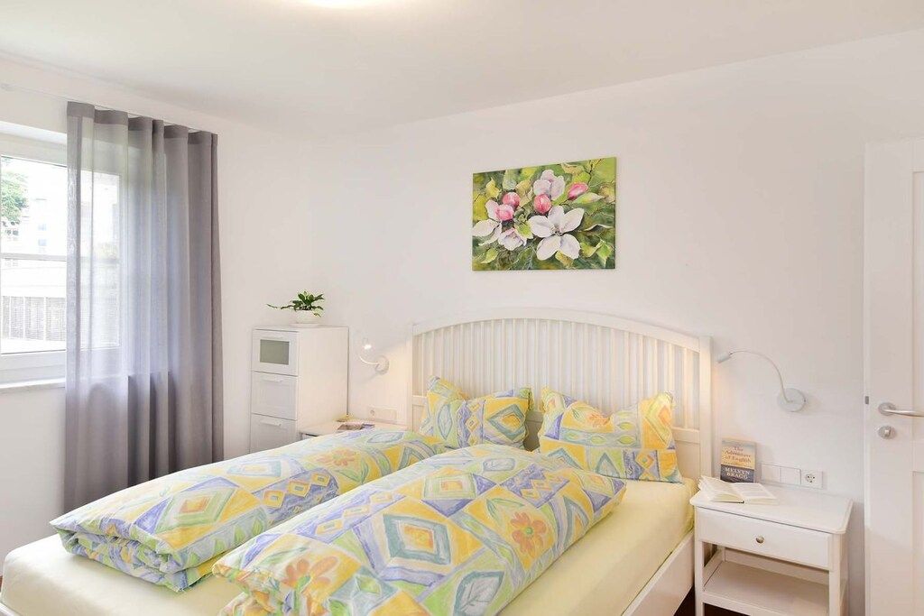 Un letto matrimoniale con biancheria a motivi decorativi, un comodino con un libro, una lampada a parete e una finestra con tende.