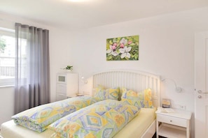 Una cama doble con ropa de cama estampada, una mesita de noche con un libro, una lámpara de pared y una ventana con cortinas.