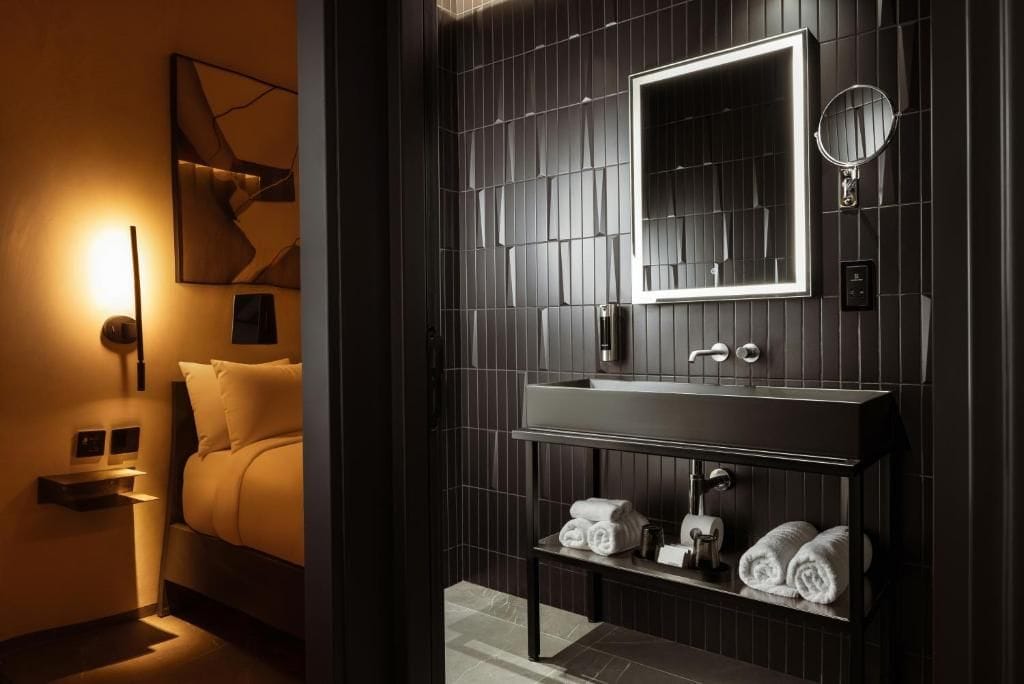 Ein modernes Badezimmer mit dunklem Holzpaneel-Design, einem großen Spiegel, einem Doppelwaschbecken und ordentlich gefalteten Handtüchern auf einem Regal.