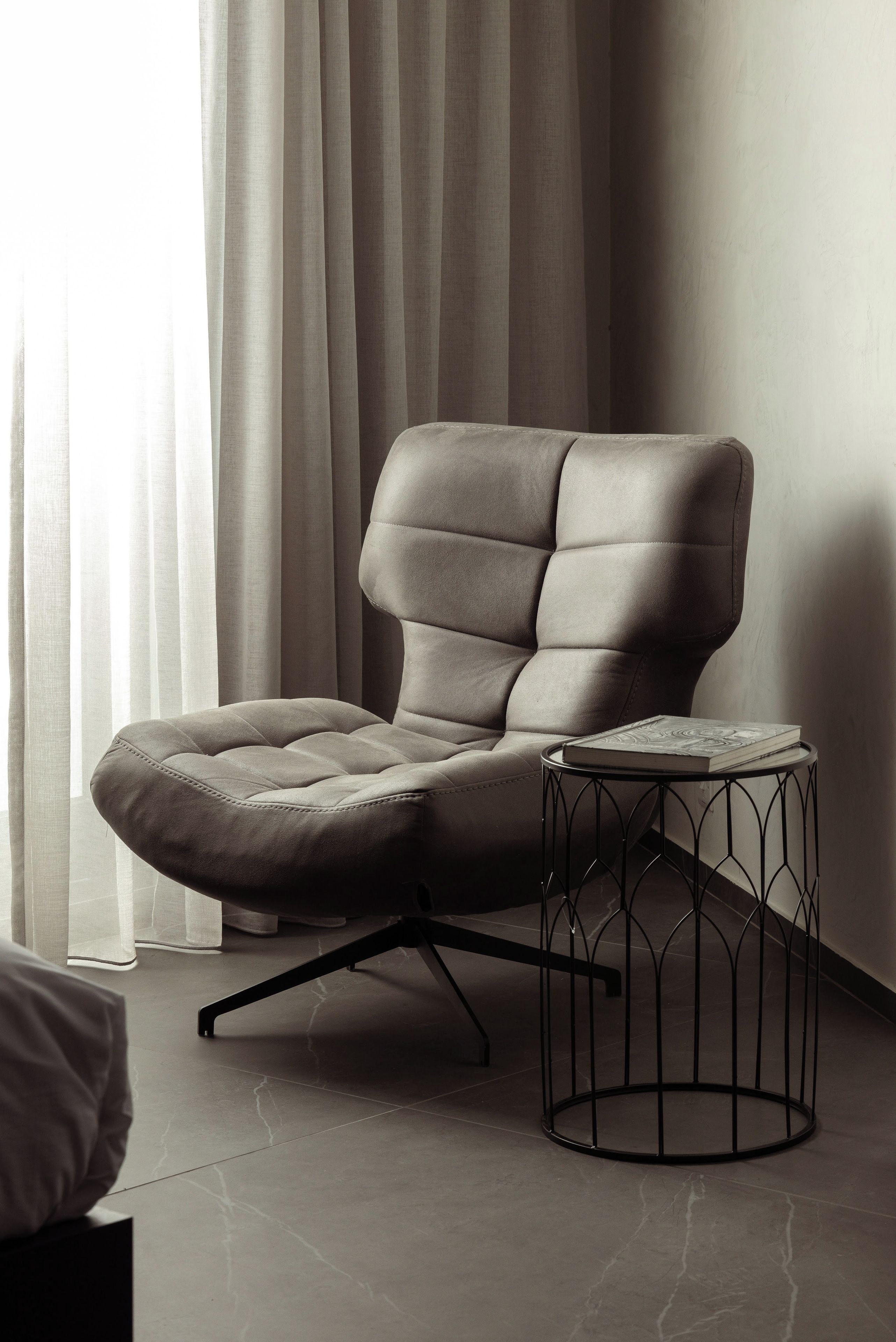 A modern chair with a cushioned seat and backrest, positioned next to a small round table with a book on it.
