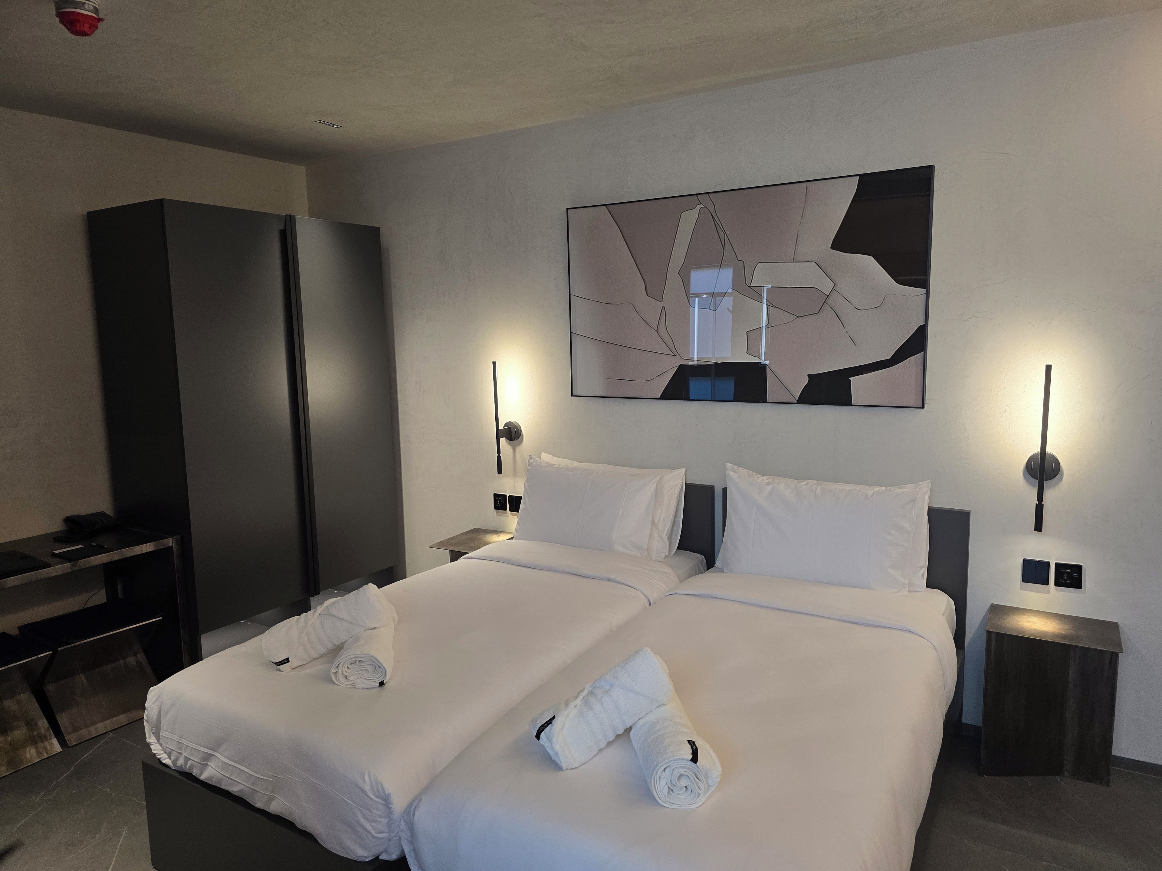 Camera d'hotel moderna con un letto grande, due comodini, una scrivania e un'opera d'arte astratta appesa al muro.