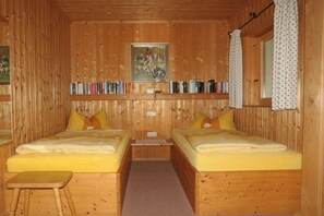 A wooden cabin room with two beds, a shelf with books, and a painting on the wall. - Holiday apartment in Bad Wiessee with parking (Bad Wiessee)