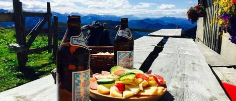A wooden table with a plate of food and two bottles of beer, set against a mountain backdrop.