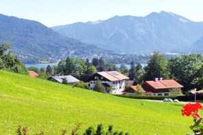Un paisaje rural con casas en una ladera, un lago y montañas al fondo.