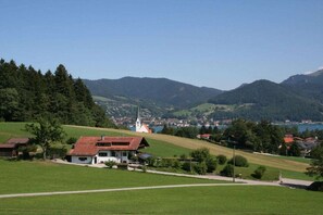 A rural landscape with a church, a house, and a view of a town across a valley. - Holiday apartment in Bad Wiessee with parking (Bad Wiessee)