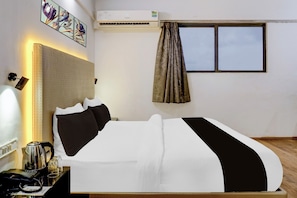 Habitación de hotel con cama, mesita de noche con teléfono y vasos, unidad de aire acondicionado y ventana con cortinas.