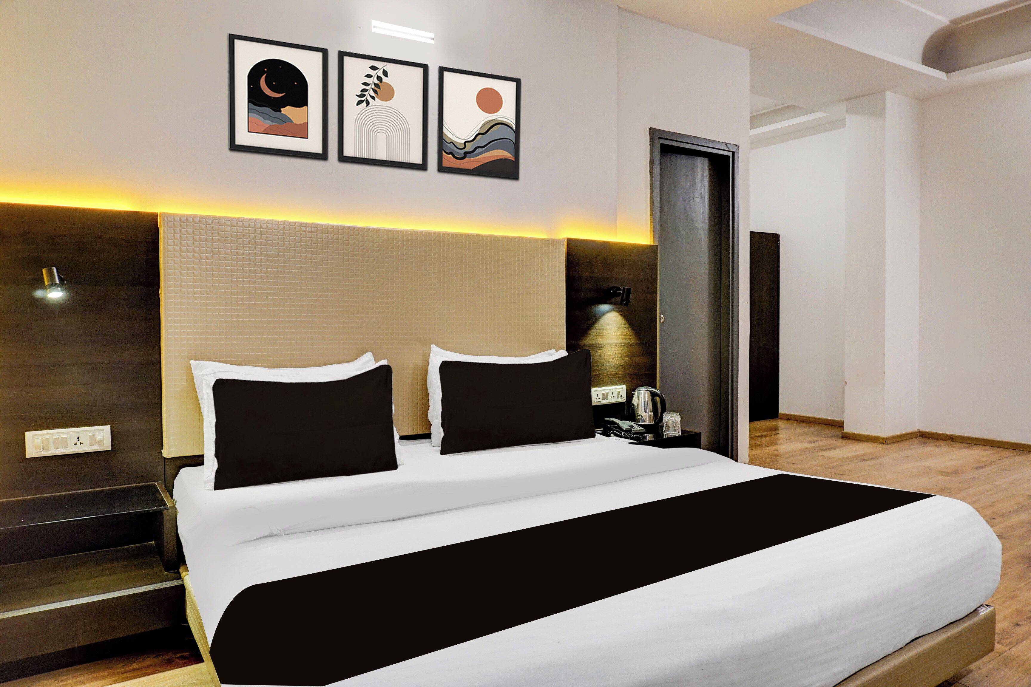 Una habitación de hotel moderna con una cama grande, una mesita de noche, una lámpara y obras de arte en la pared.