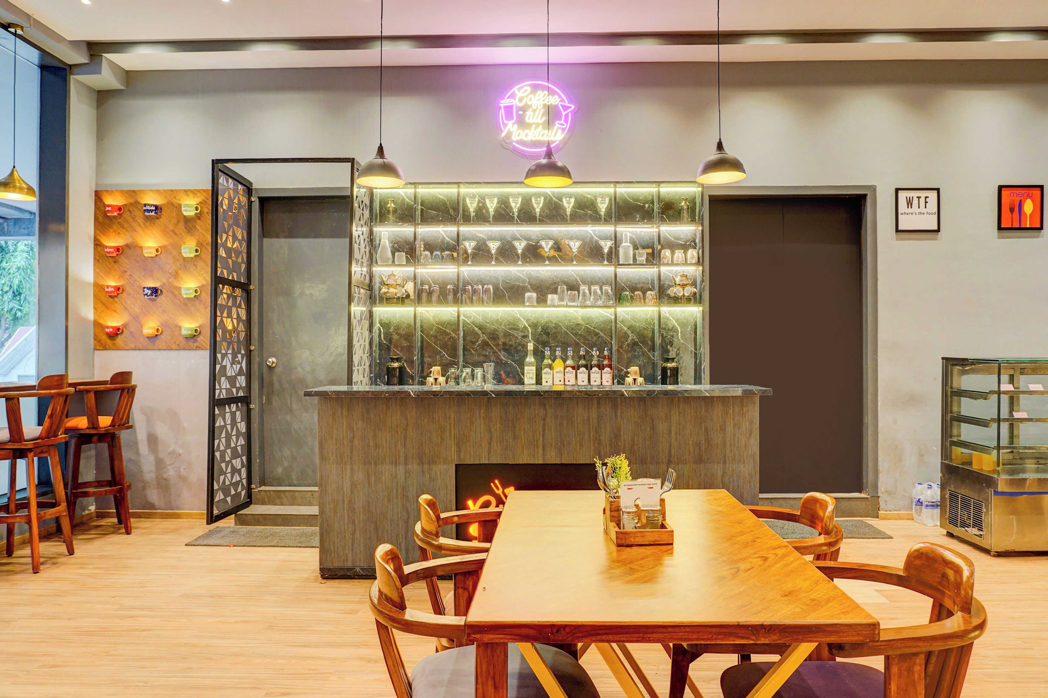 Interior de un restaurante con barra, sillas de madera y un letrero de neón.