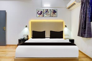 A hotel room with a bed, bedside lamps, a nightstand, a power outlet, and a wall-mounted air conditioner.