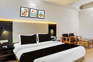 Una habitación de hotel moderna con una cama grande, dos almohadas negras, una mesita de noche, una mesita con lámpara, una silla de madera y una pequeña mesa con un vaso.