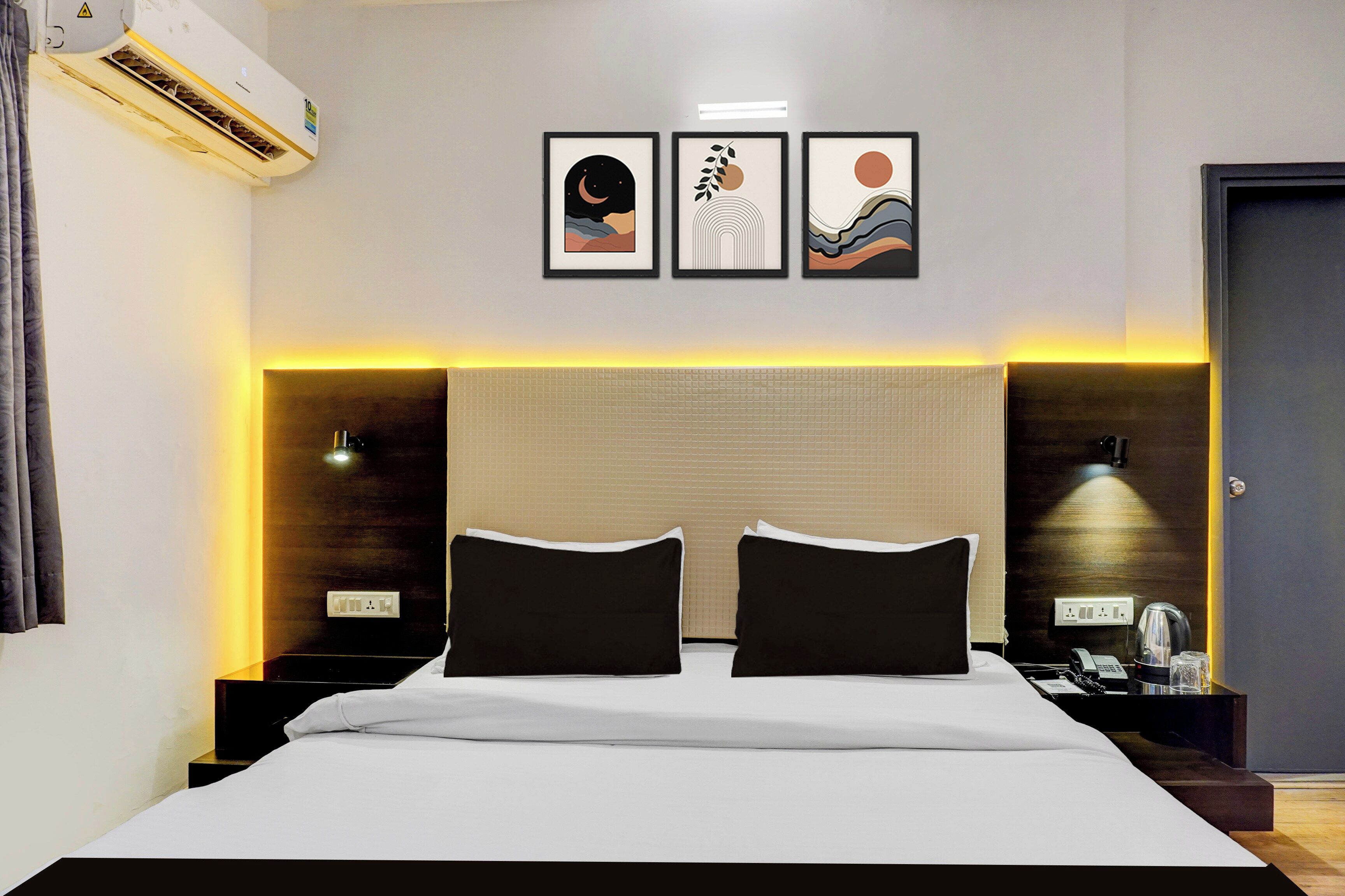 Habitación de hotel con una cama grande, dos mesitas de noche, un equipo de aire acondicionado y tres cuadros en la pared.
